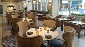 Un restaurant amb taules rodones, cadirees amb coixí i llums penjants.