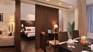 Habitació d'hotel amb un llit, un escriptori amb un ordinador, una taula de menjador preparada per a dues persones i una cadira.