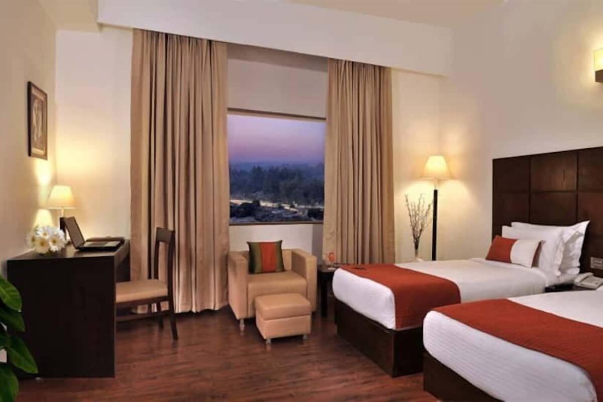 Ein Hotelzimmer mit zwei Betten, einem Schreibtisch, einem Stuhl und Blick auf die Stadt.
