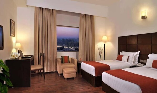 Una habitación de hotel con dos camas, un escritorio, una silla y vistas a la ciudad.