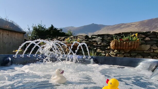 Ein Whirlpool mit zwei Gummientchen, einer Steinmauer und einem Holzzaun im Hintergrund.