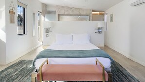 Un dormitorio moderno con una cama grande, una banca, un espejo y vistas al exterior.