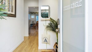 Un corridoio con pavimento in legno, un'opera d'arte incorniciata a sinistra, uno specchio sulla parete e una porta con la scritta 'URBAN JUNGLE'.