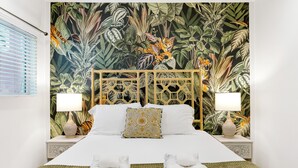 Un letto con carta da parati a tema tropicale, due abat-jour e un cuscino decorativo.