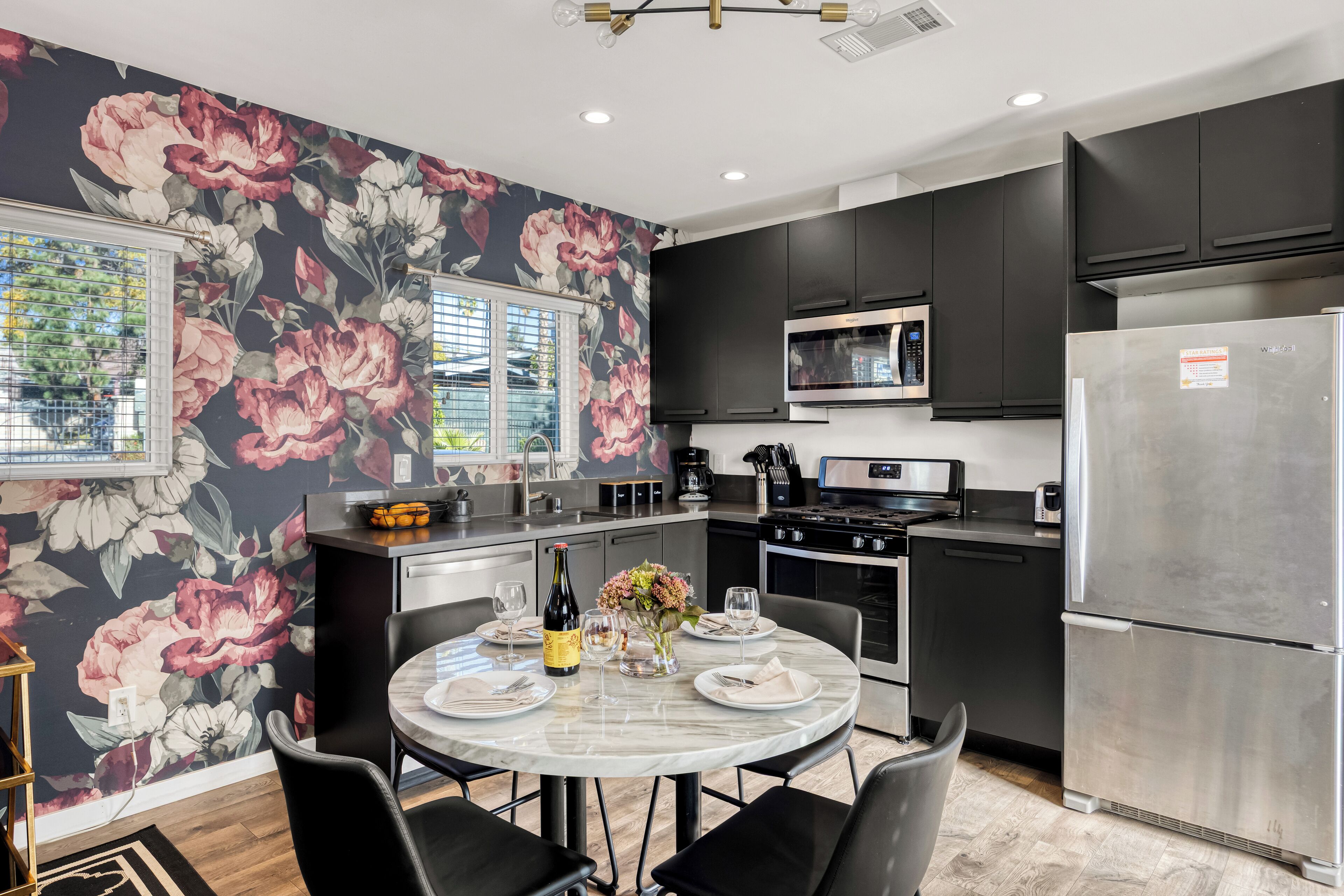 A modern kitchen with dark cabinets, a stainless steel refrigerator, and a dining area with a round table set for four.