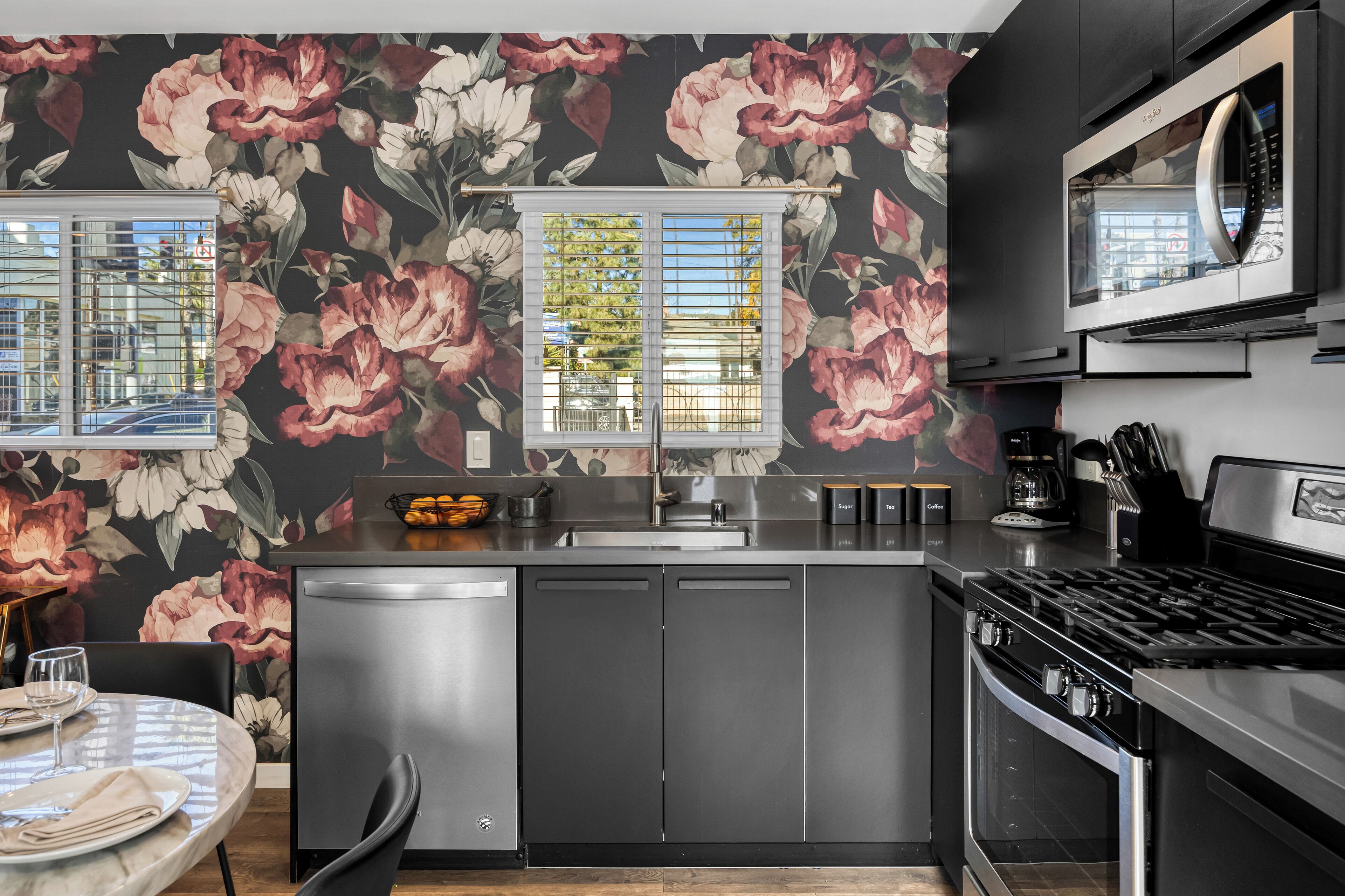 A modern kitchen with a central island, stainless steel appliances, and a floral wallpaper design.