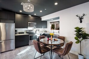 A modern kitchen with dark cabinets, stainless steel appliances, and a dining area with leather chairs. - Vibey 2BDR in Prime Hollywood | Steps to Attractions | Rock n Roll by AvantStay (Los Angeles)