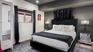 Un dormitorio con una cama grande, un armario, una mesita de noche con lámpara y una ventana con cortinas.