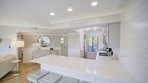 Une cuisine moderne dotée d’un îlot central, de meubles blancs et d’une enseigne indiquant « MAISON DE PLAGE ».