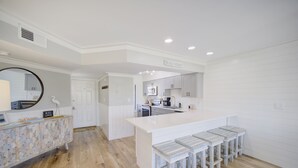 Une cuisine avec des meubles blancs, un grand îlot central doté de tabourets, et un pare-feu avec un motif géométrique.