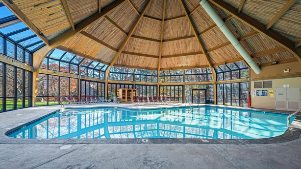 Ein großer Innenpool mit Holzboden und Glaswänden, umgeben von Liegestühlen.