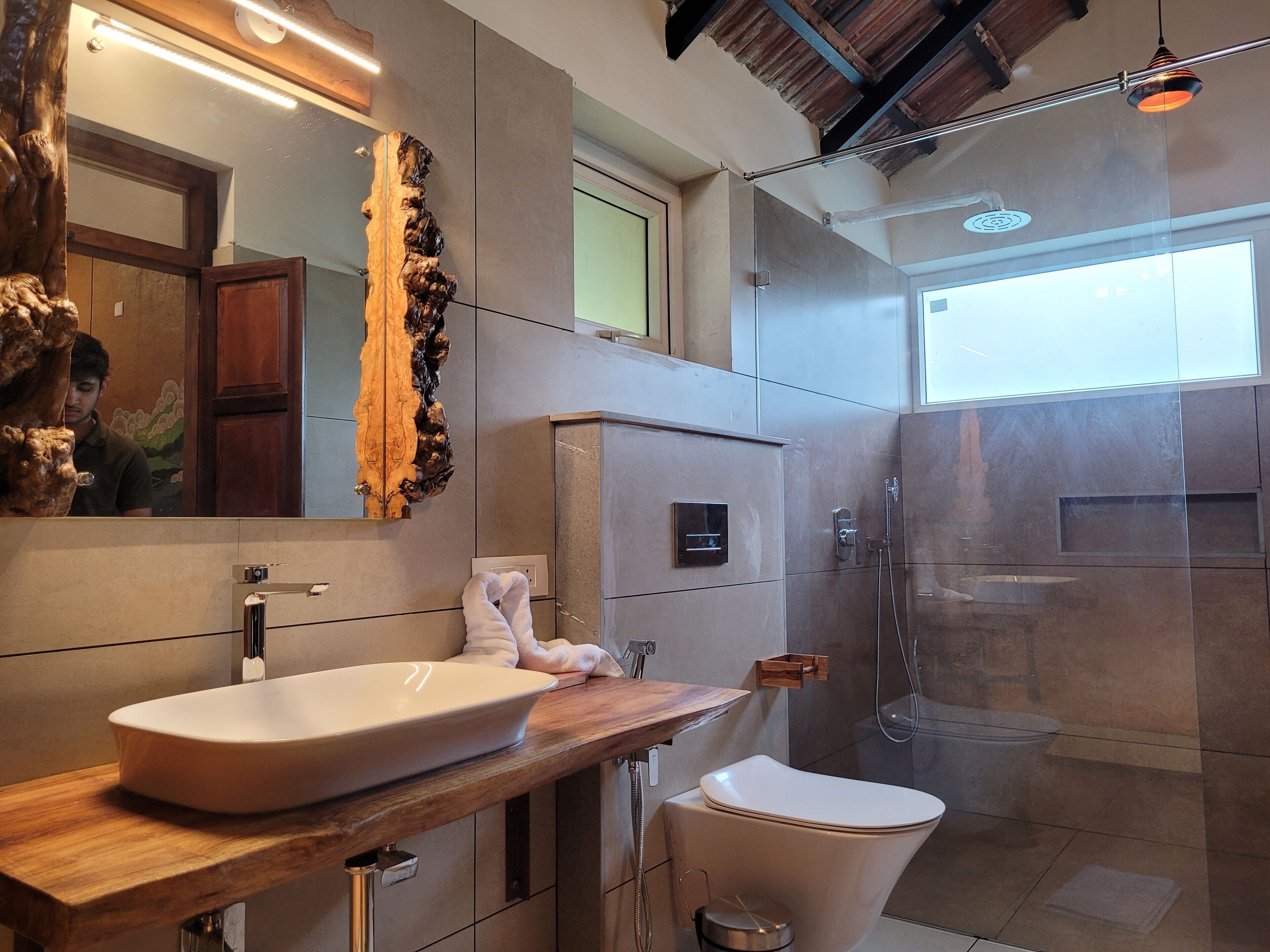 A modern bathroom with a large mirror, a wooden vanity, a white sink, a toilet, and a glass-enclosed shower area.