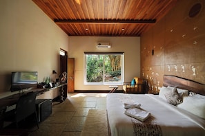 A bedroom with a large bed, a desk with a TV, a window with a view of greenery, and a wooden ceiling. - Aalterra Resort by The Almanac (Vythiri)