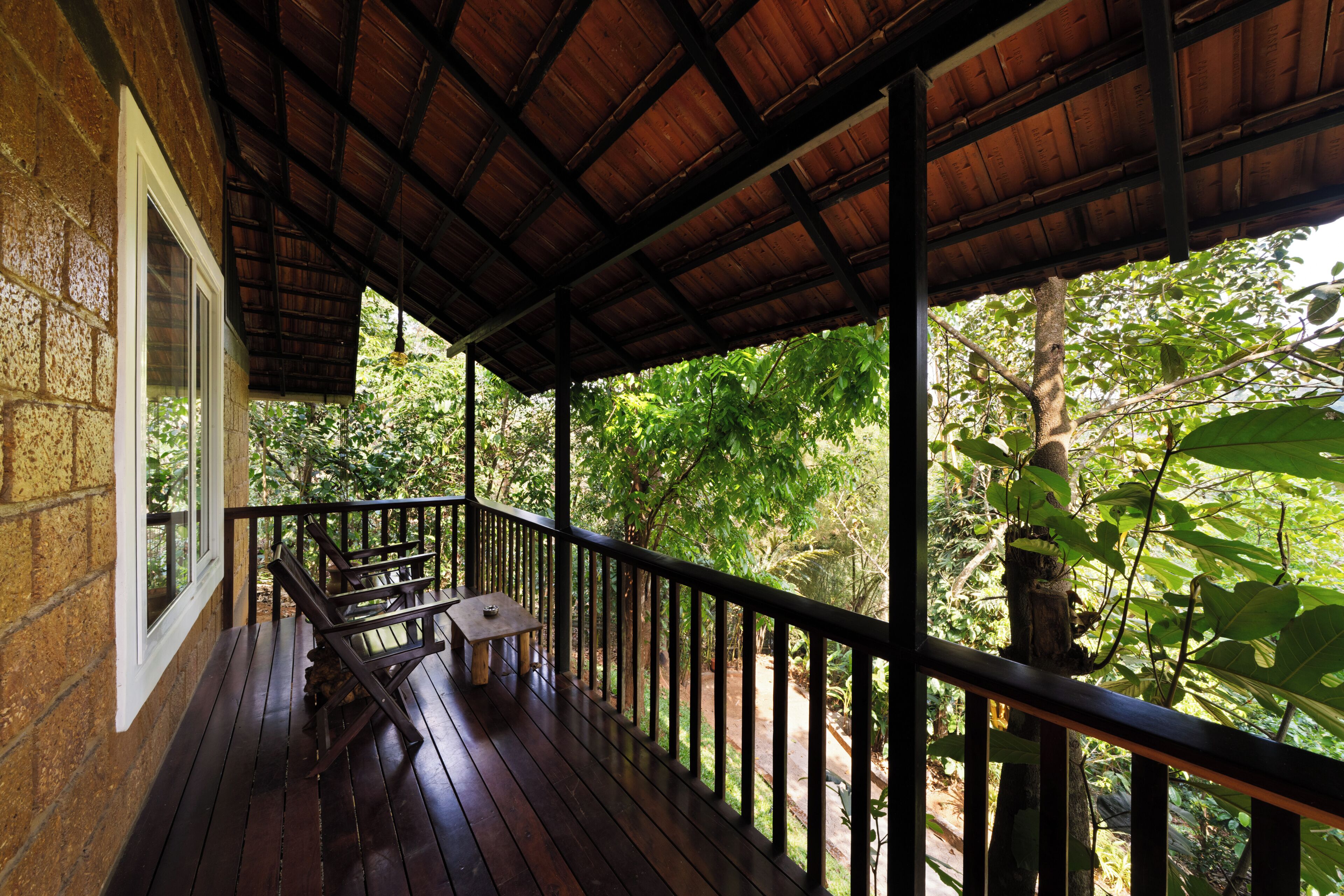 A covered wooden deck with a bench and table, overlooking a lush green forest.
