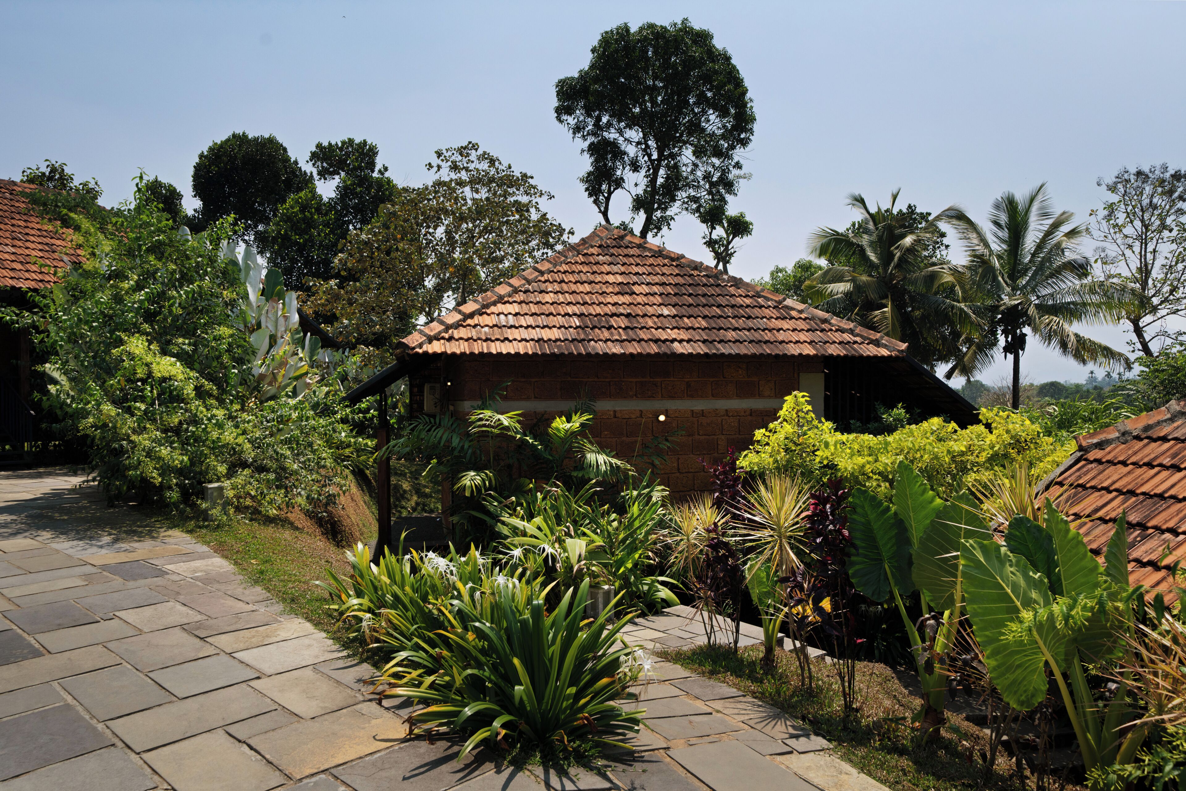 A brick building with a tiled roof, surrounded by lush greenery and palm trees.