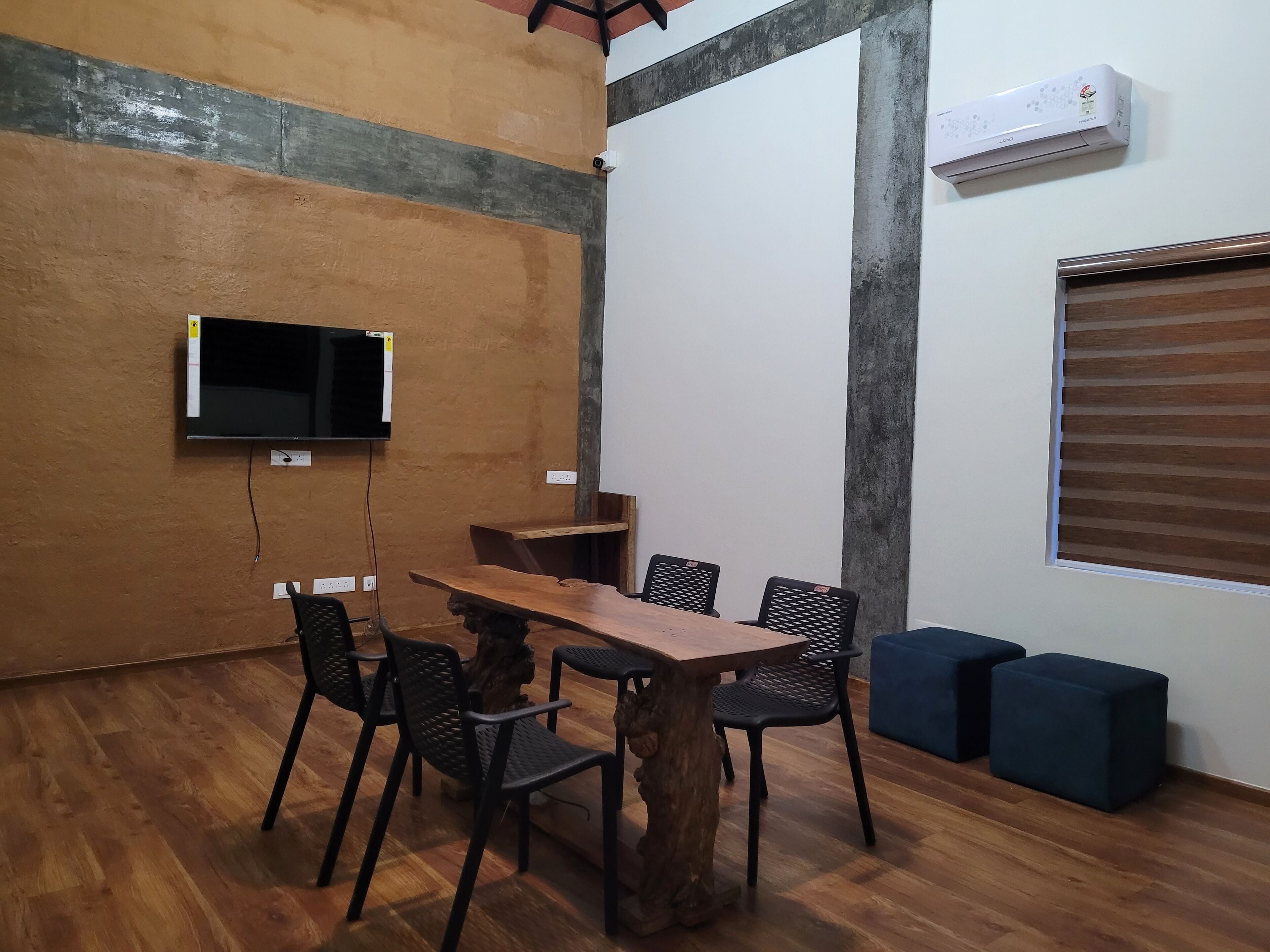 Een vergaderruimte met een houten tafel, zwarte stoelen met mesh-net, een vastgeschroefde flatscreen-tv en een airconditioner aan de muur.