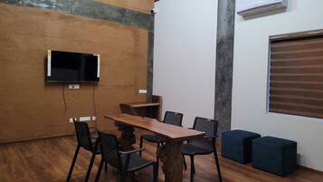 Een vergaderruimte met een houten tafel, zwarte stoelen met mesh-net, een vastgeschroefde flatscreen-tv en een airconditioner aan de muur.