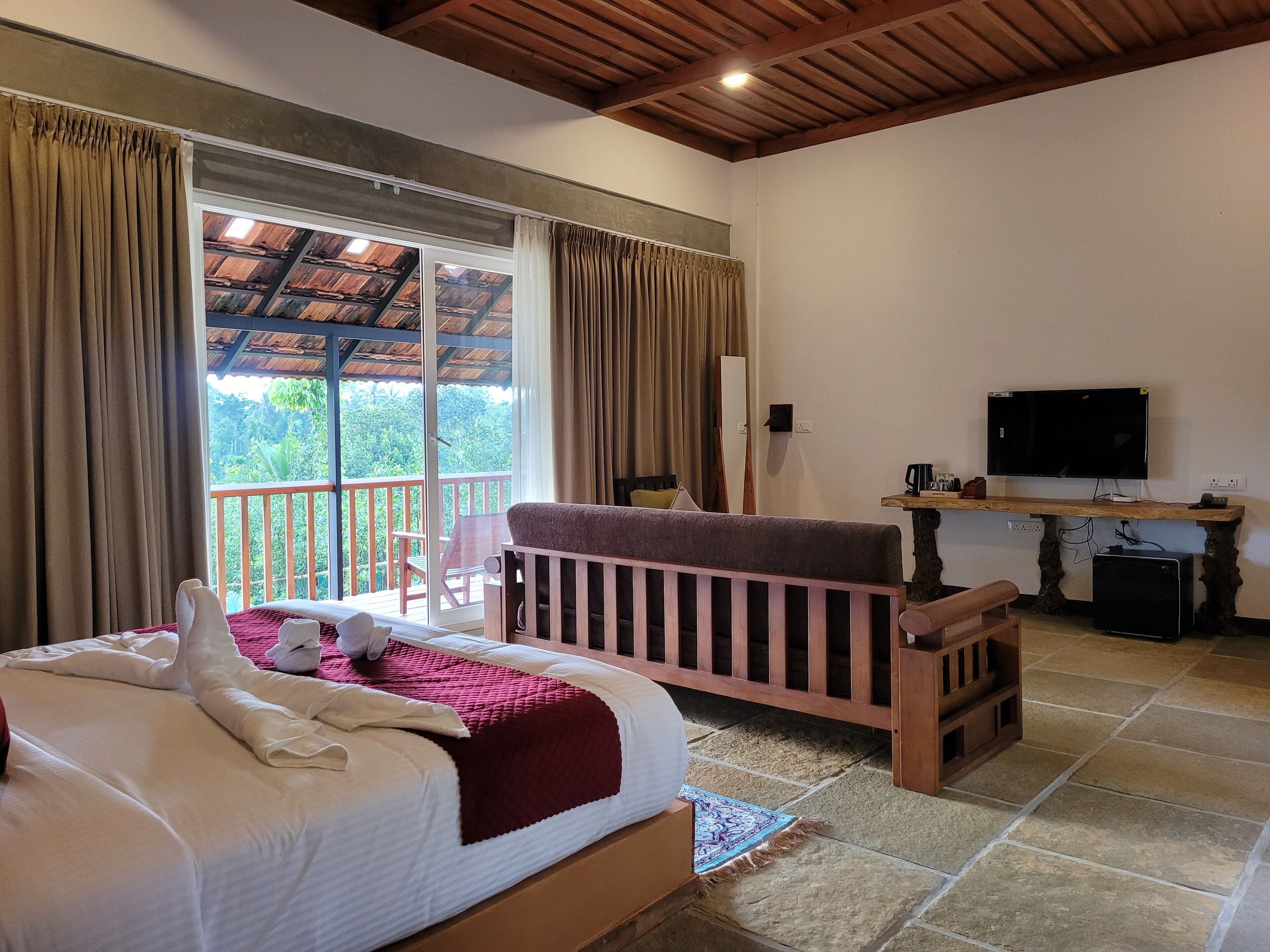 A bedroom with a large bed, a wooden crib, a TV, and a balcony with curtains.