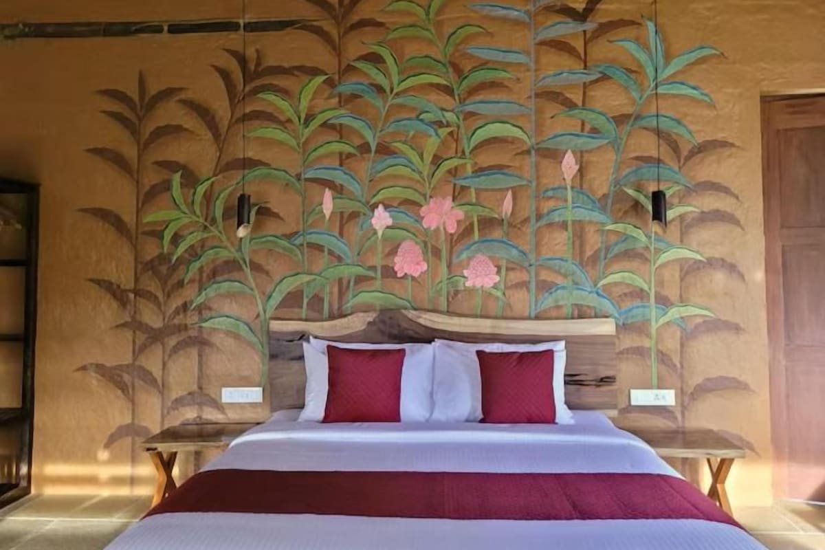 A bed with a headboard, pillows, and a blanket in a room with a wall mural.