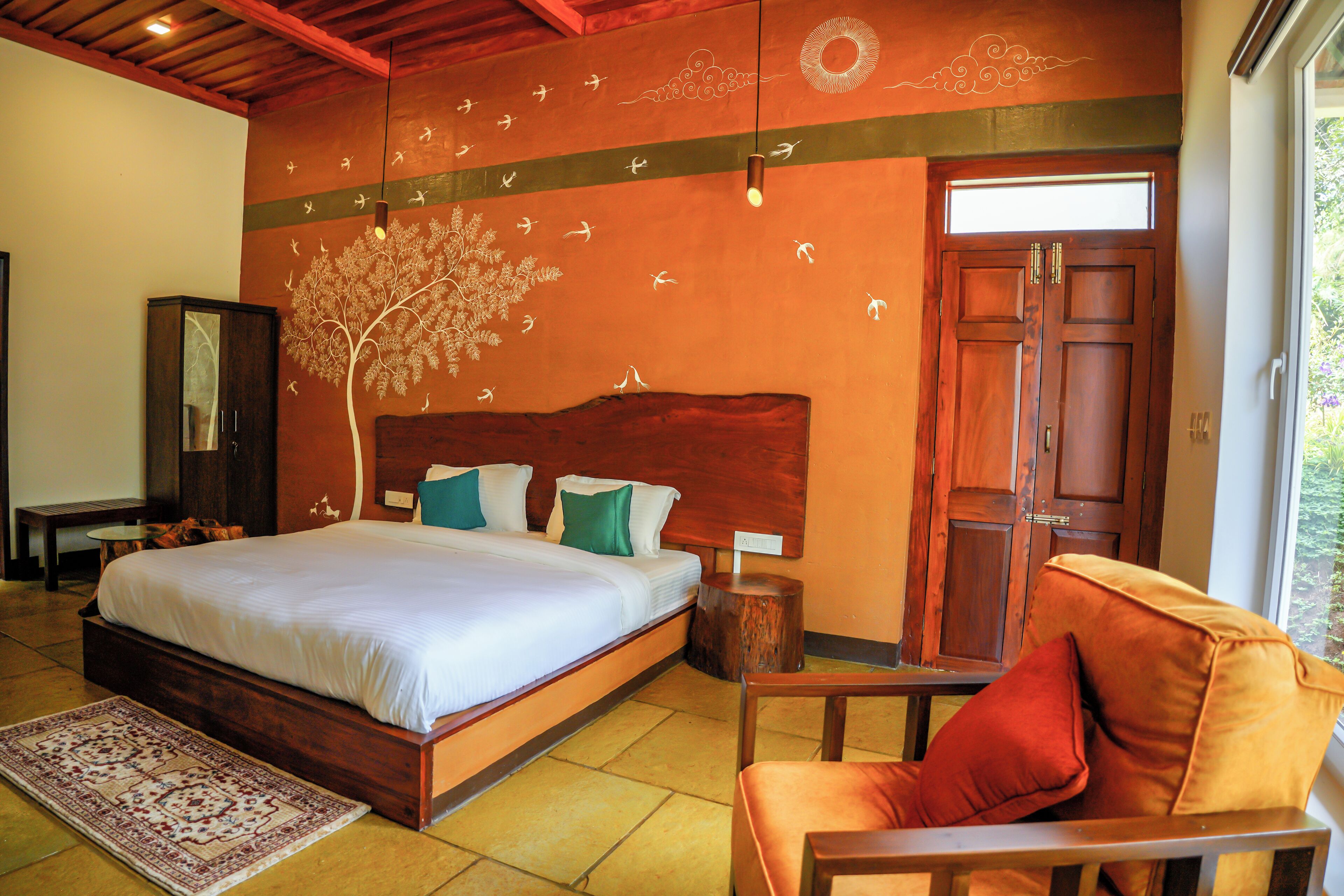 Un dormitorio con una cama grande, cabecera de madera, mesita de noche, una silla y un mural en la pared.