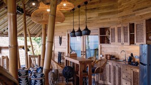 Un interior de madera con zona de cocina, columnas de bambú, lámparas de fibra y decoración tradicional.