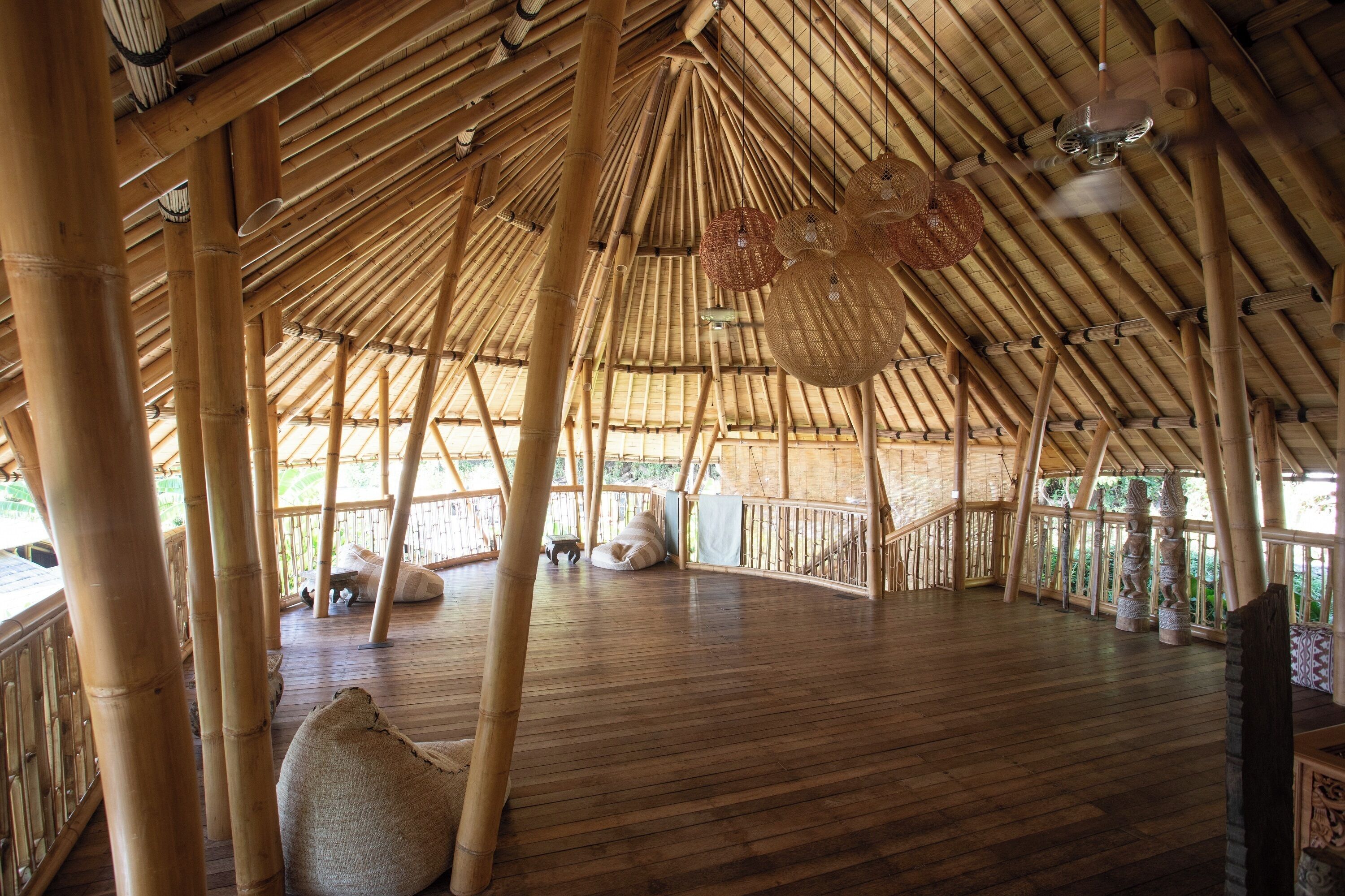 A spacious bamboo structure with a wooden floor, large woven baskets hanging from the ceiling, and a railing along the perimeter.