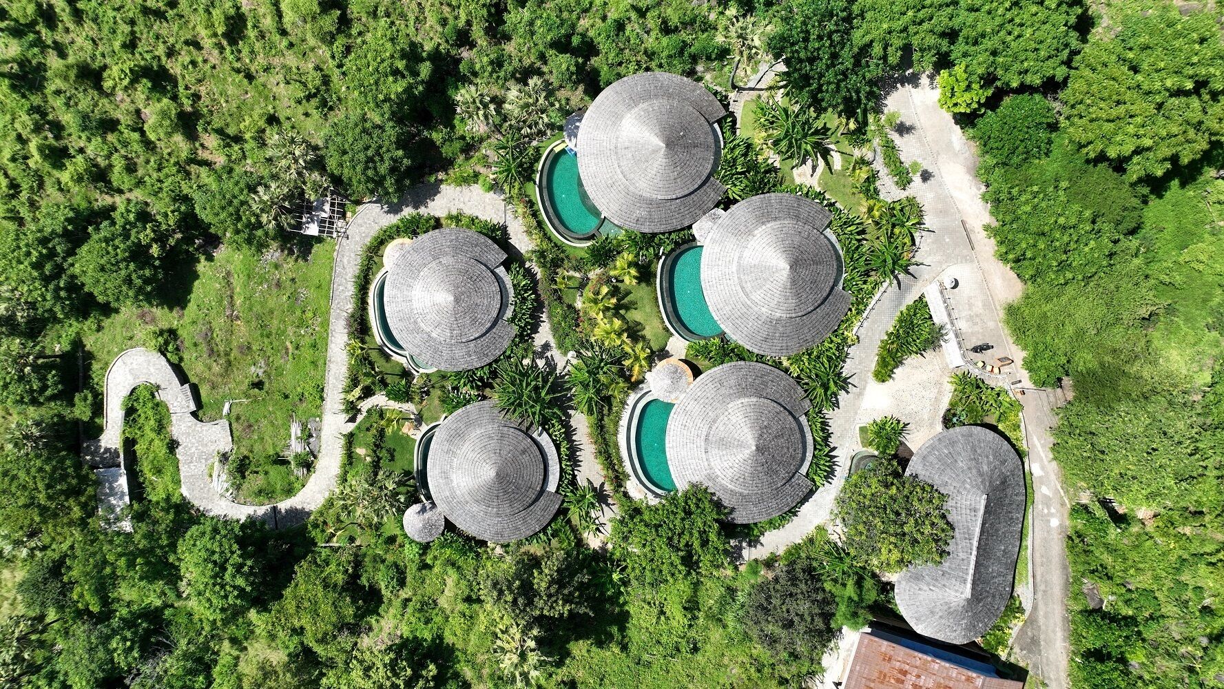 An aerial view of a resort with multiple dome-shaped buildings, surrounded by lush greenery and a winding pathway.