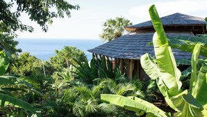 A tropical setting with a wooden structure surrounded by lush greenery and a view of the ocean. - Villas Bukit Lipah (Karangasem)
