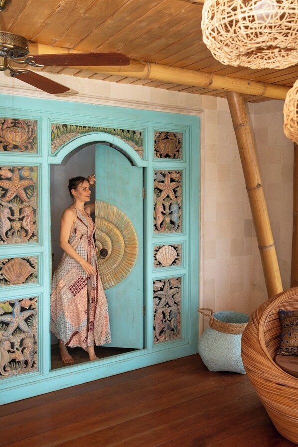 A room with a blue door featuring intricate carvings, a ceiling fan, and a woven rattan chair. - Villas Bukit Lipah (Karangasem)