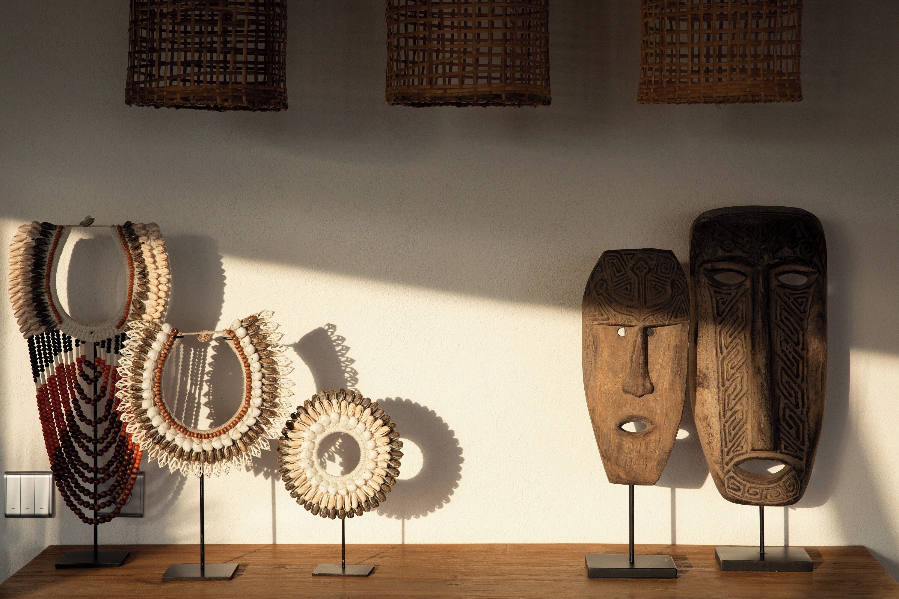 Ausstellung traditioneller Masken und verzihlter Halsketten auf Ständern vor einer Wand.