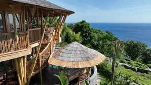 A bamboo structure with a thatched roof overlooking a lush landscape and the ocean. - Villas Bukit Lipah (Karangasem)