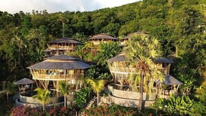 A resort with multiple circular wooden structures surrounded by lush greenery and a hillside backdrop. - Villas Bukit Lipah (Karangasem)
