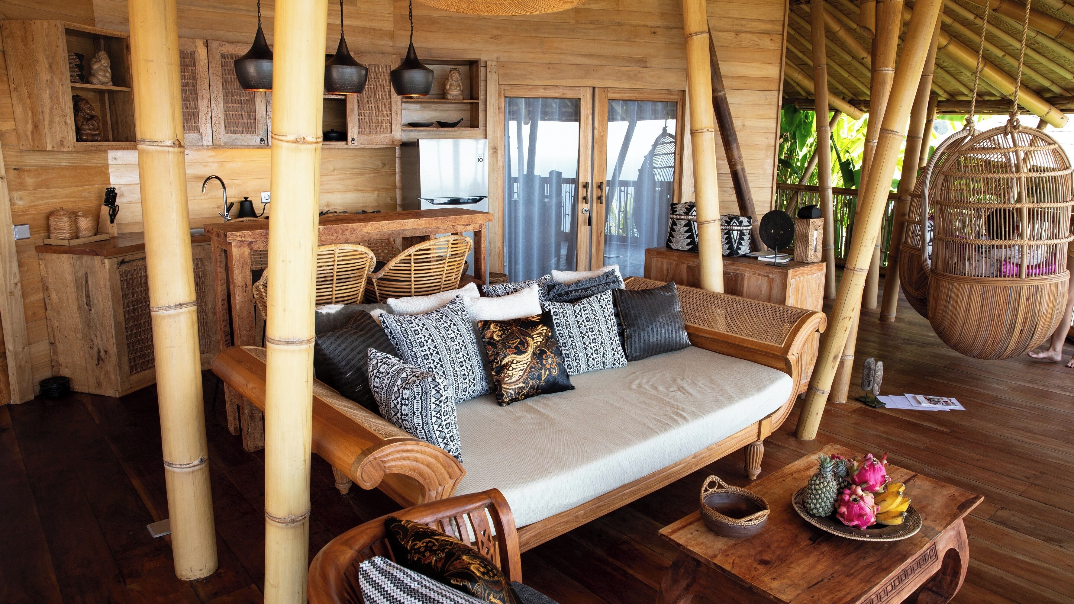 A bamboo-themed room with a sofa, wicker chairs, and a dining table with fruit.