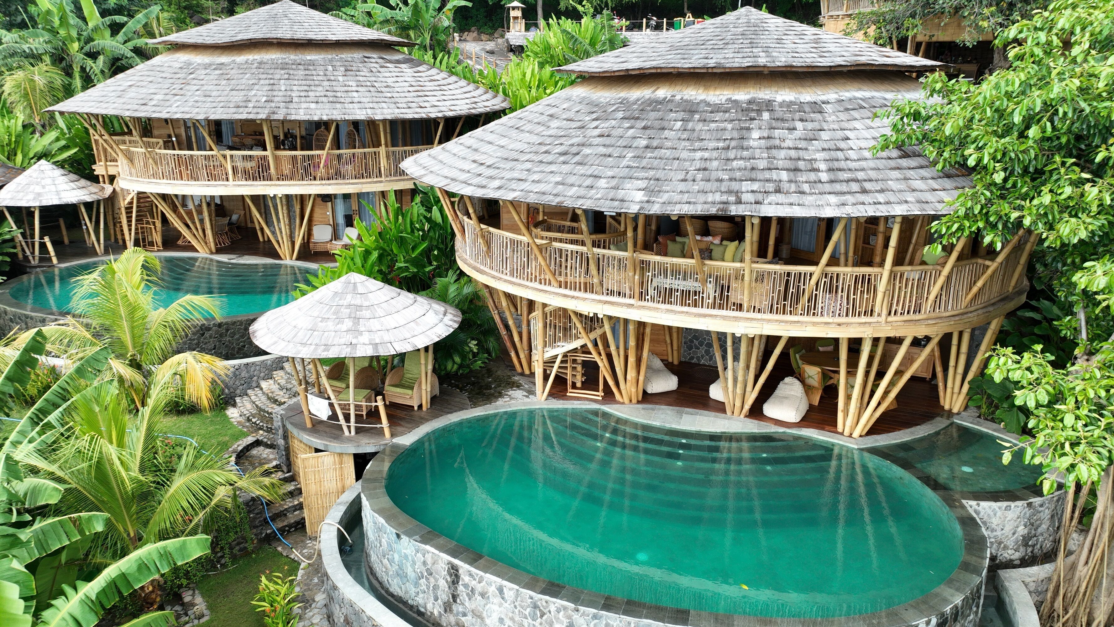 Un resort con varias piscinas circulares y estructuras de bambú con zonas de estar.