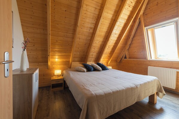 Un dormitorio con techo de madera, una cama con almohadas, una mesita de noche, un aparador y una ventana.