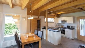 Una cocina moderna con vigas de madera, un comedor con mesa y sillas, y vistas a zonas verdes.