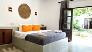 A modern bedroom with a large bed, a round woven wall hanging, and a view of a garden through a sliding door. - Lum Residence (Ahangama)