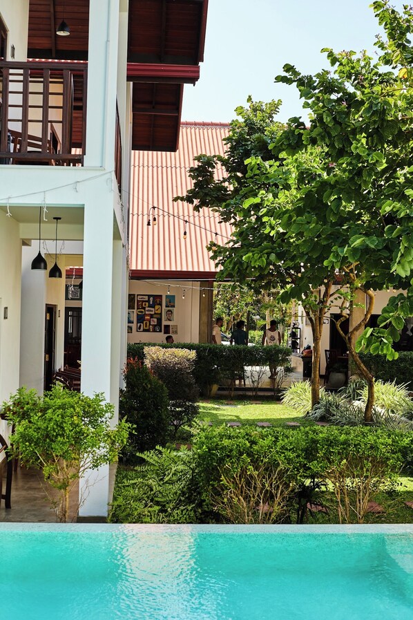 A pool area with a view of a building with a red roof and a balcony. - Lum Residence (Ahangama)