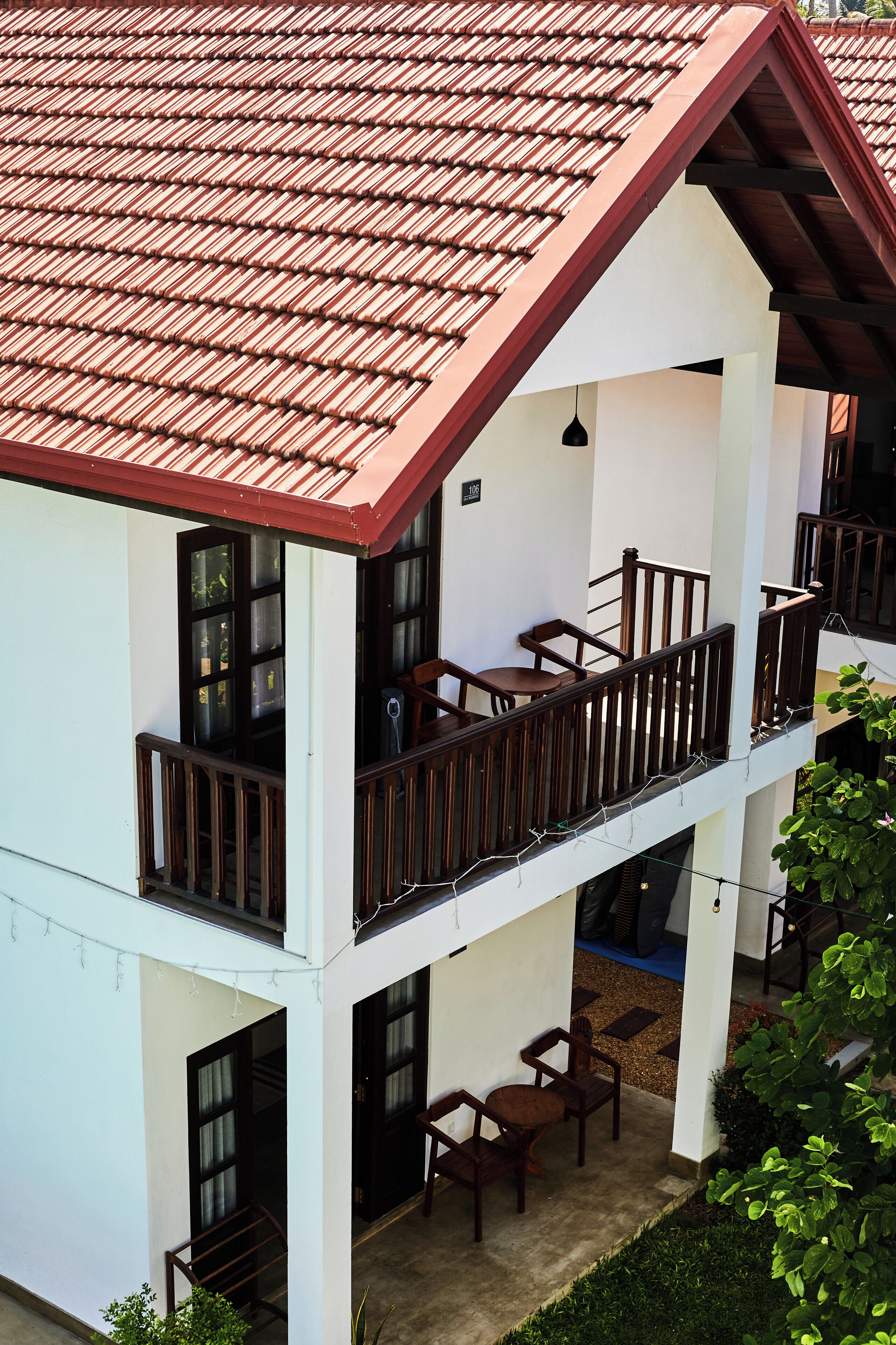A two-story building with a red-tiled roof, balconies with wooden railings, and a courtyard with outdoor seating.
