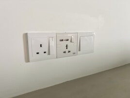 Una toma de corriente blanca con tres enchufes, un puerto USB e interruptor en una pared lisa.