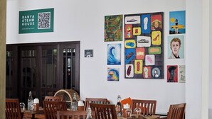 A dining area with wooden tables and chairs, a QR code sign, and various artworks on the wall. - Lum Residence (Ahangama)