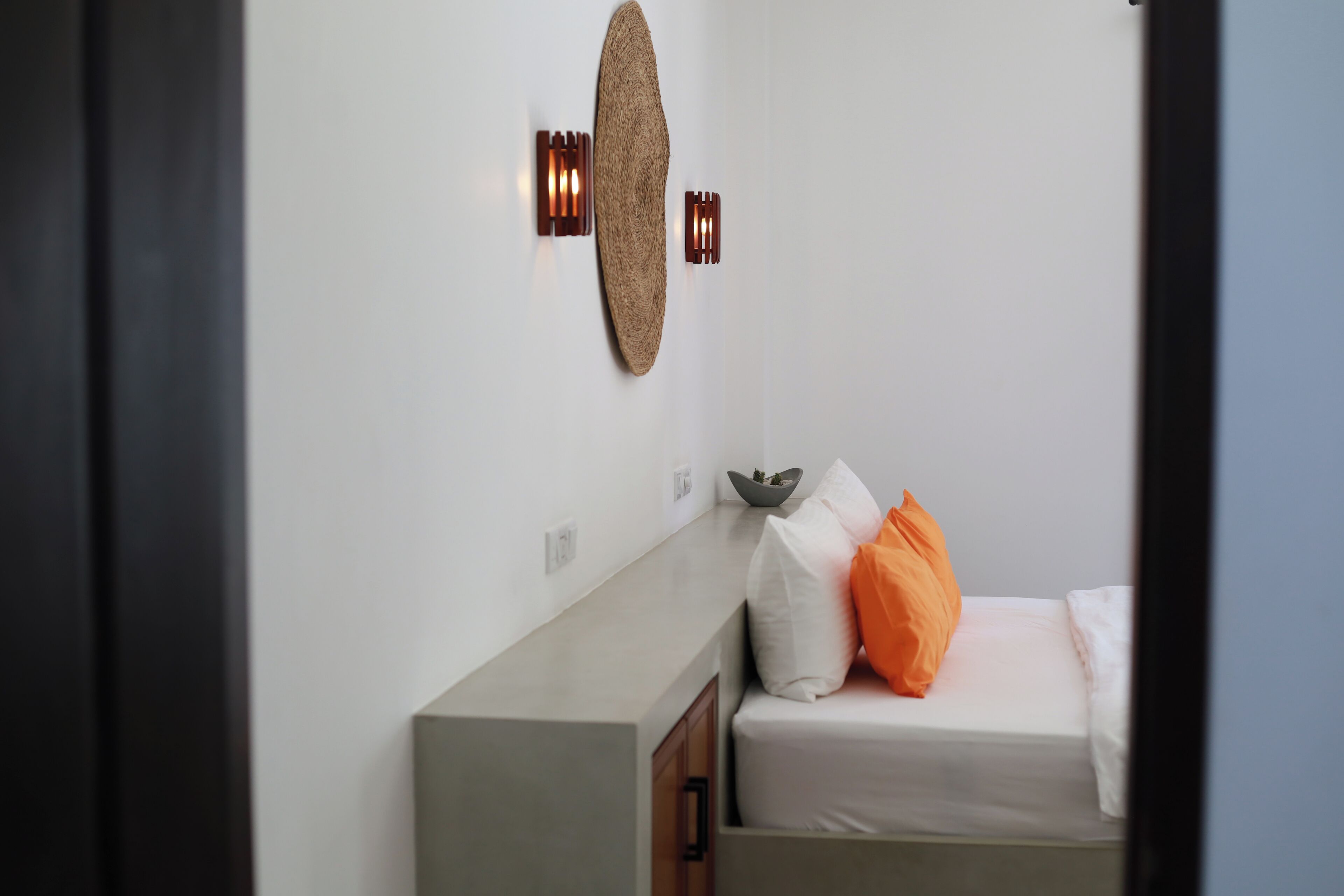 Una camera da letto con un letto, cuscini, un punto luce a parete e un tavolino con una ciotola.