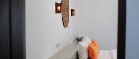 Una camera da letto con un letto, cuscini, un punto luce a parete e un tavolino con una ciotola.