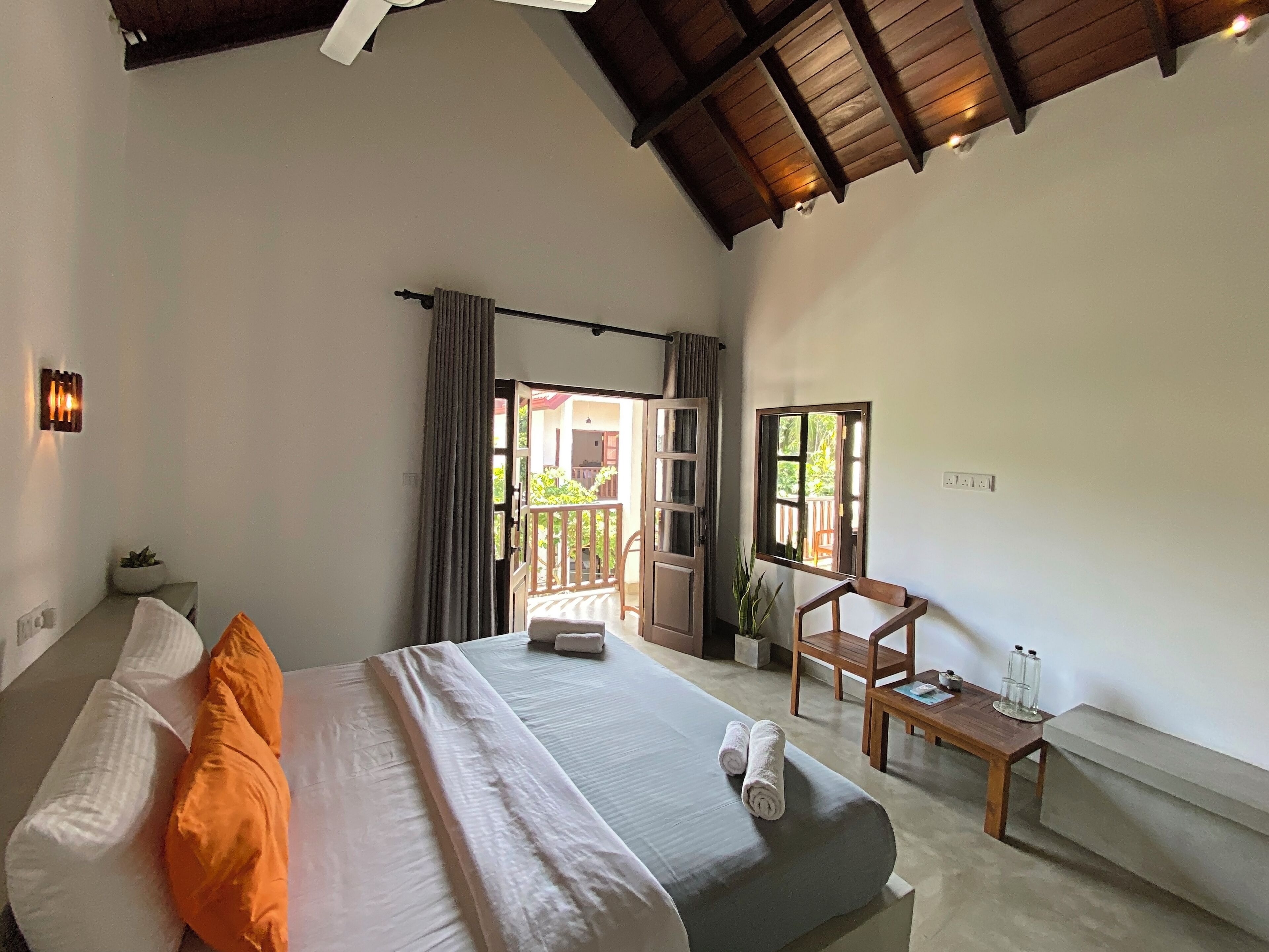 A bedroom with a bed, pillows, a wooden chair, a small table, and a window.