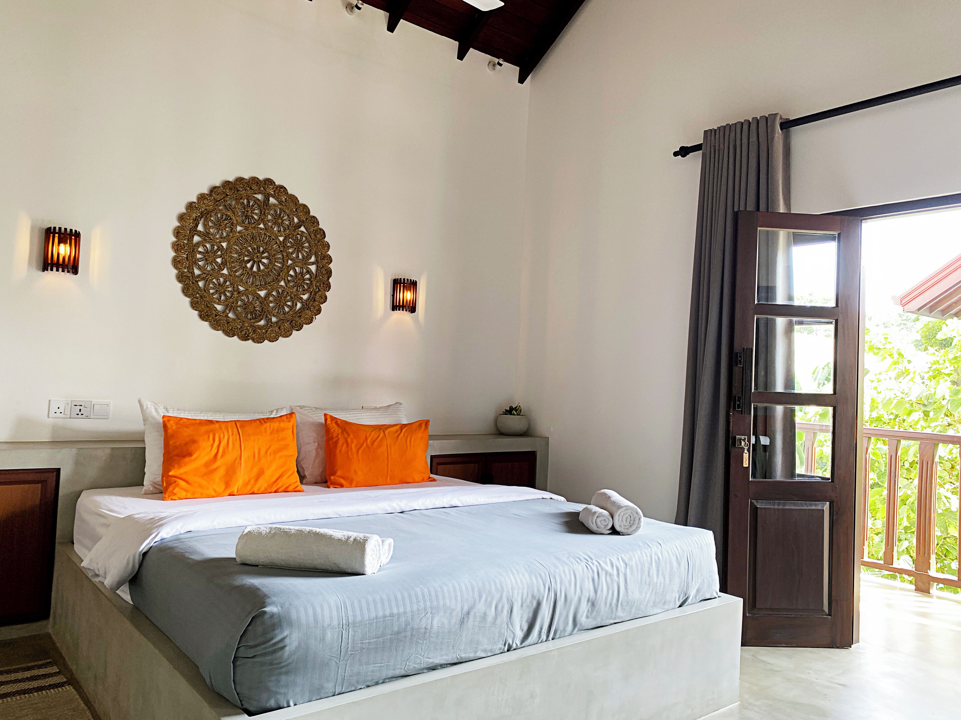 A bedroom with a bed, two wall sconces, a decorative wall piece, and a door leading to an outdoor area.