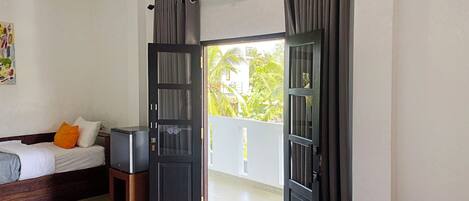 A hotel room with a bed, a small table, a TV, and a balcony with curtains.