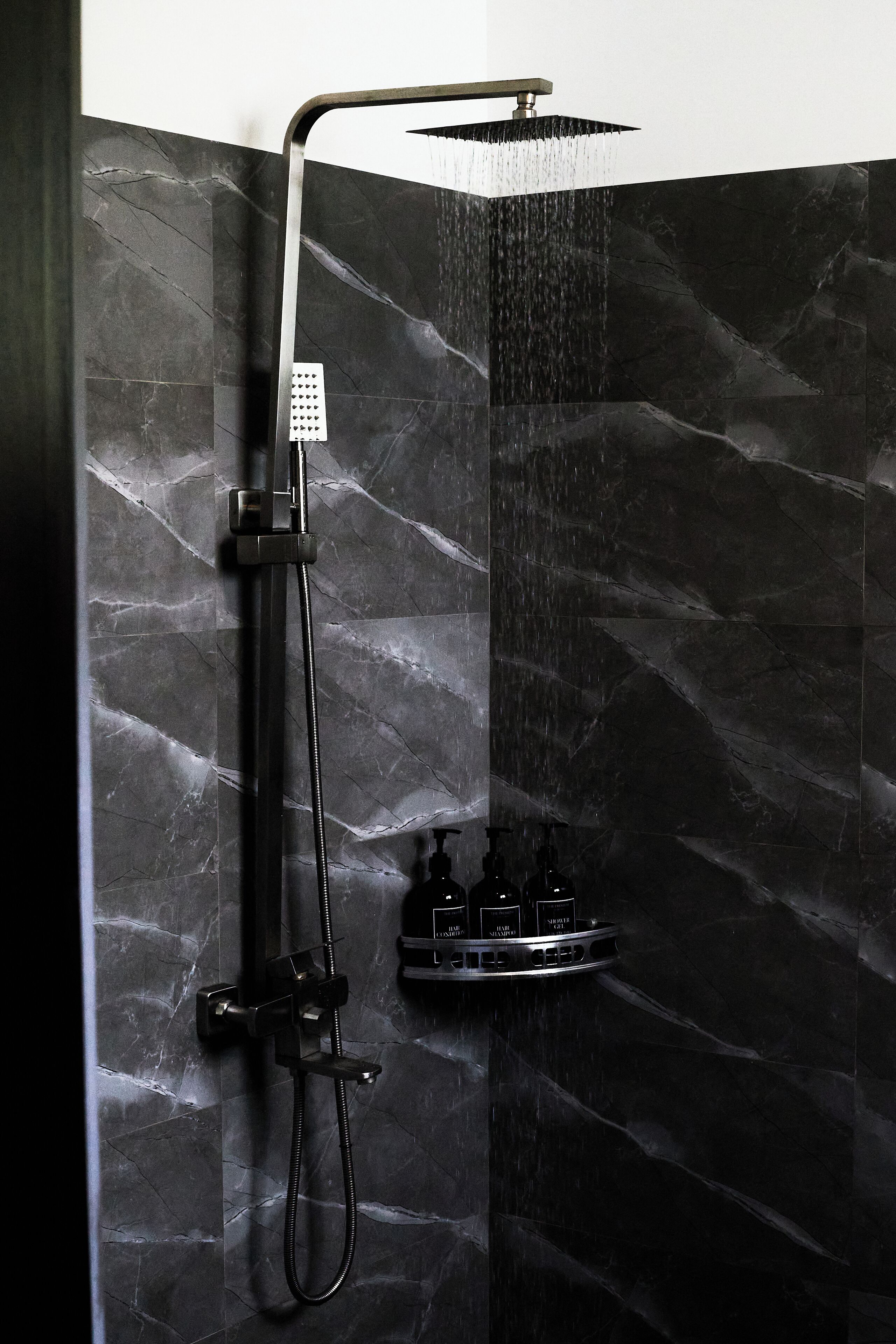 Moderni suihku, jossa on sekä ylhäältä alas suihkuttava suihkupää että käsisuihkupää, ja taustalla on tumma marmoriseinä.