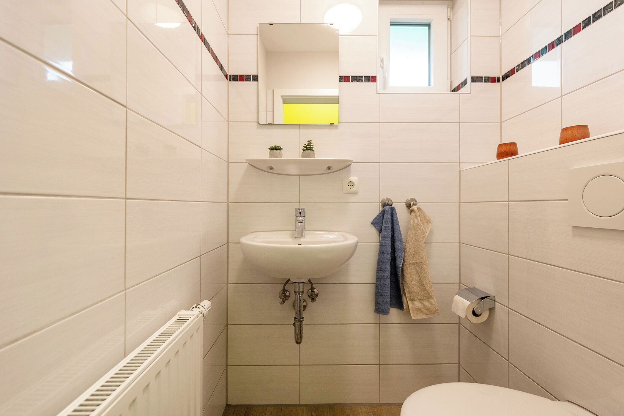 Ett litet badrum med ett vitt handfat, en spegel, en handdukshängare och en toalett.