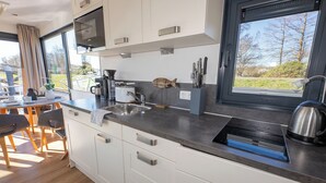 Een moderne keuken met witte kasten, een roestvrijstalen spoelbak en een groot raam met uitzicht op de omgeving.