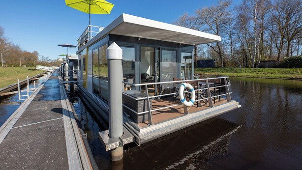 Een moderne drijvende constructie met een overdekt dek, glazen wanden en een reddingsboei.